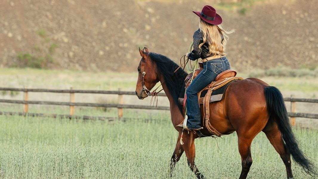 A woman in western dress rides her horse across open grass.